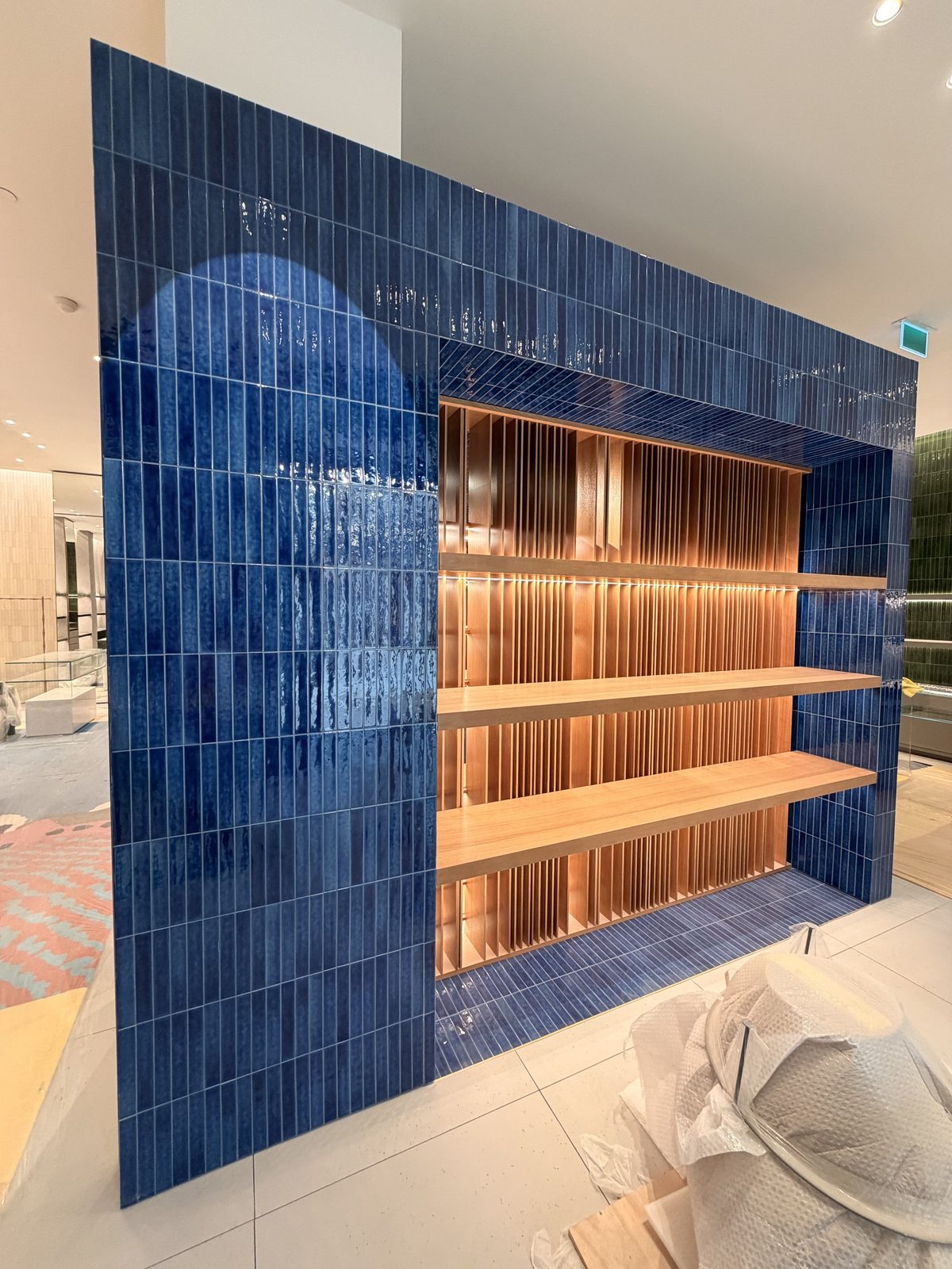 Deep blue glazed tile feature wall with lit wood shelving at Oakridge Centre